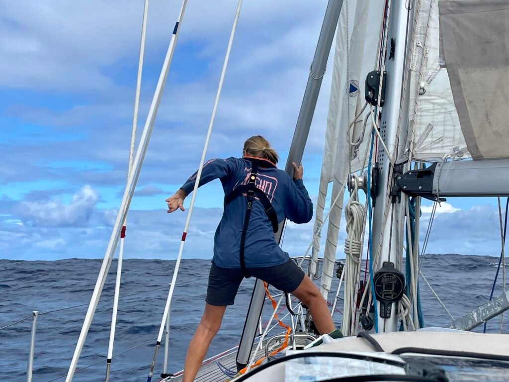 Sailor adjusting a spinnaker pole while sailing offshore on a Rustler 36 yacht in open ocean conditions.