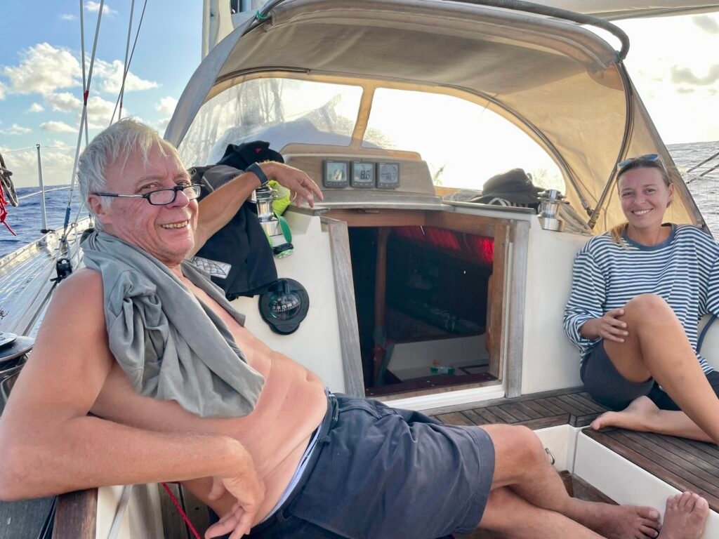 Two sailors relaxing on a yacht while crossing the Pacific Ocean double-handed, navigating open ocean conditions on an offshore sailing passage.